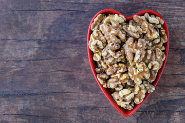 Toasted walnuts in a red heart shaped ceramic bowl on a rustic background
