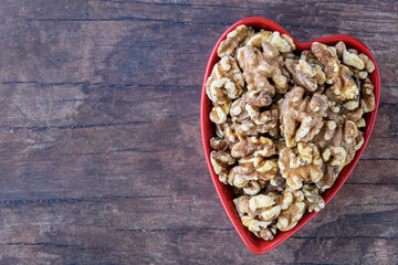 Toasted walnuts in a red heart shaped ceramic bowl on a rustic background

