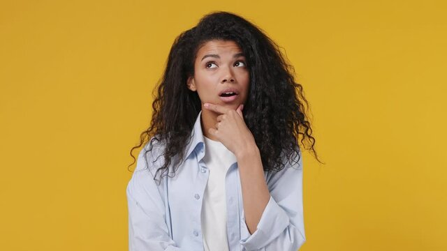 Fun confused shy shamed young african woman curly hair 20s years old wears blue white t shirt look camera spreading hands say oops ouch oh omg i am so sorry isolated on yellow color wall background