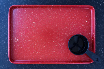 Red baking sheet with a black measuring cup on a black background
