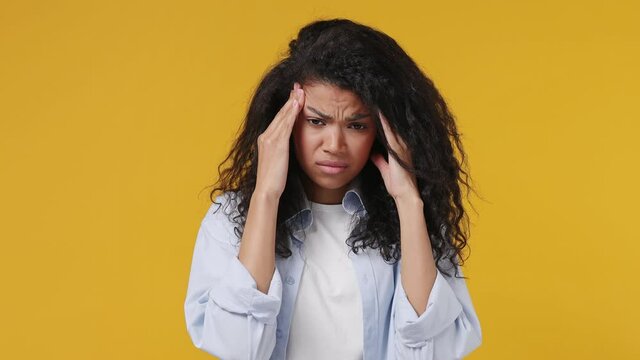 Sick ill sad tired young african woman wear blue white t shirt put hands on head rub temples having headache suffering from pain migraine feel bad seedy isolated on yellow color wall background studio