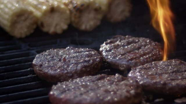 Close up slow motion shot of flames shooting up from juicy burgers on the grill