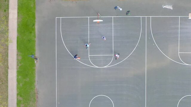 Top down aerial of young men, boys playing basketball. Shooting hoops. Teenager dribbles ball and approaches basketball backboard and net.