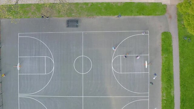 Full basketball court top down aerial shot. Male players shoot baskets and three pointers in USA.