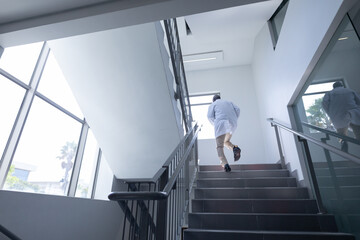 Senior african american male doctor wearing lab coat running up stairs in hospital - Powered by Adobe