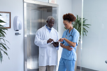 Diverse male and female doctors using tablet and discussing in hospital corridor
