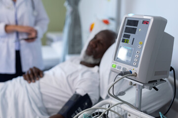 African american male patient lying on hospital bed next to blood pressure monitor