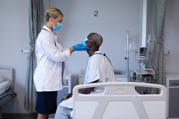Fototapeta premium Caucasian female doctor wearing face mask palpating lymph nodes of african american male patient
