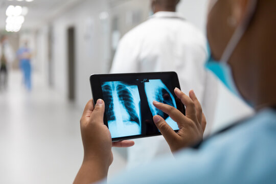 Mixed Race Doctor In Corridor Wearing Face Mask Looking At Lung X-ray On Tablet