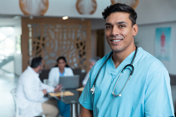 Portrait of smiling mixed race male doctor with colleagues in discussion in the background - Powered by Adobe