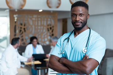 Portrait of african american male doctor smiling, with colleagues in discussion in the background