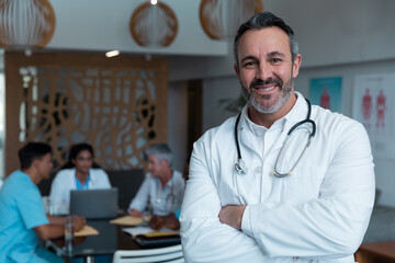 Portrait of smiling caucasian male doctor, with colleagues in discussion in the background