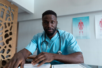 Fototapeta premium African american male doctor at desk talking and gesturing during video call consultation