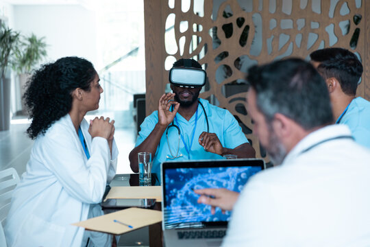 Diverse Male And Female Doctors Wearing Face Masks Sitting At Table And Using Vr Glasses