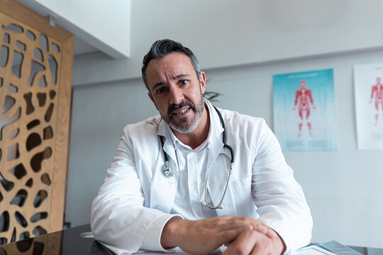 Mixed race male doctor at desk talking and gesturing during video call consultation
