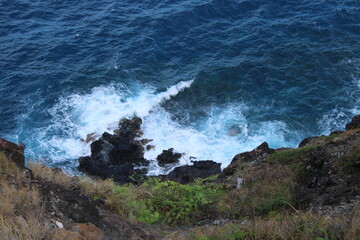 Looking down a cliff to see waves crashing against the rocks below on Oahu, Hawaii.