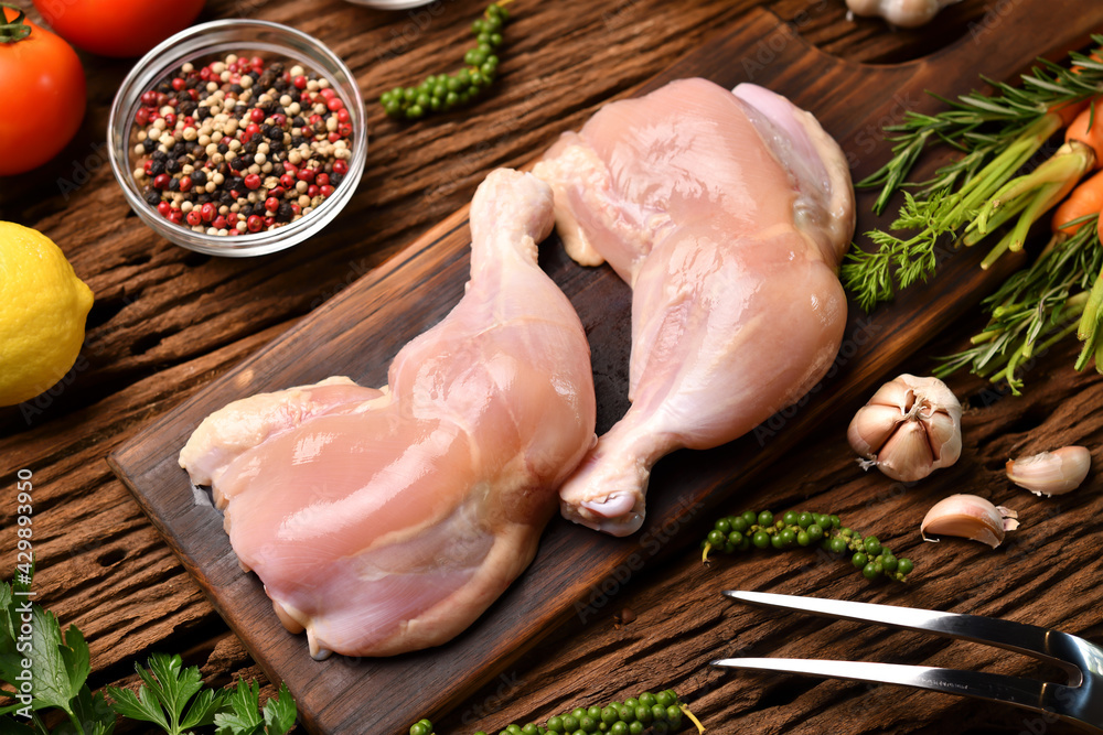 Wall mural skinless raw chicken thighs with ingredients for cooking on a wooden cutting board