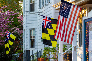 Historical Colonial Era Maryland Flag Calvert Arms Kings Colors featuring checkered yellow and black banner of Lord Baltimore and a Union Jack is hanging side by side with a US flag on a building - obrazy, fototapety, plakaty