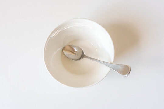 High angle closeup of empty ceramic bowl with spoon on white background (selective focus)
