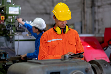 Factory worker man hold tablet and inspect the function while her co-worker work with other machine in the background. Maintenance and check system support industrial business.