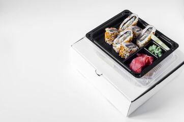 fresh fish cucumber and cheese rolls decorated with sesame seeds. Wasabi and ginger rolls in a dark plastic bowl and cardboard box top view. food delivery concept