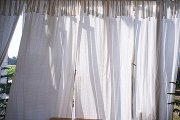 Long, white, semy see-through curtains hanging in the window,Sun shining through curtain,Curtains on window with sun,The sun shines through curtains at sunset close up,interior details.