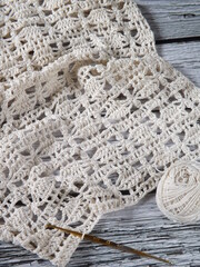 Unfinished crochet project using white yarns as material, following certain pattern in mixed stitches. Laid on white rustic wooden table. Concept of art, hobby, recreation, and creativity.