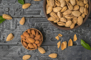 Peeling almonds from their shells on a black wooden table. Flat lay.