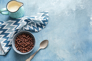 Bowl with chocolate corn balls and jug of milk on color background