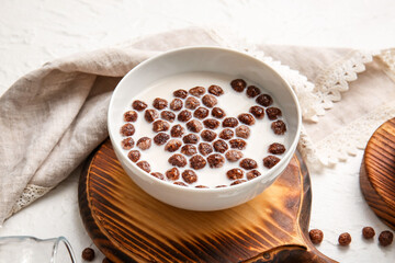 Bowl with chocolate corn balls and milk on light background