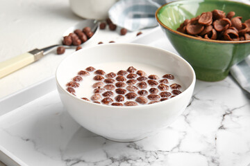 Bowls with chocolate corn balls and milk on light background