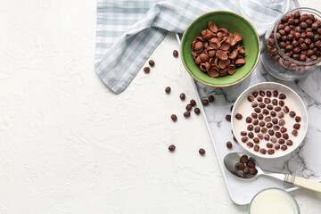 Bowls with chocolate cornflakes and milk on light background