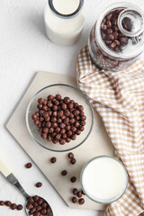 Bowl with chocolate corn balls and glass of milk on light background
