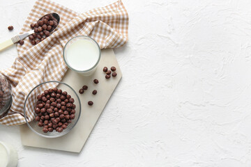 Bowl with chocolate corn balls and glass of milk on light background