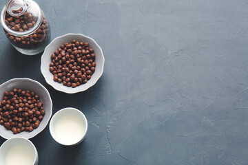 Bowl with chocolate corn balls and glasses of milk on dark background