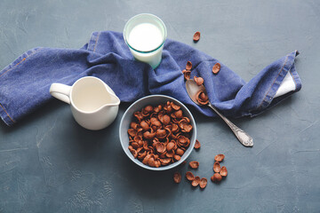 Bowl with chocolate cornflakes and jug of milk on dark background