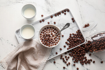 Bowl with chocolate corn balls and milk on light background