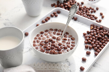 Bowl with chocolate corn balls and milk on light background