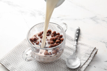 Pouring of milk into bowl with chocolate corn balls on light background