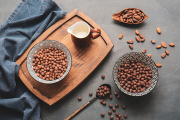 Bowls with chocolate corn balls and jug of milk on grey background