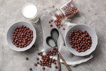 Bowls with chocolate corn balls and glass of milk on grey background