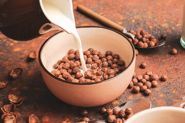 Pouring of milk into bowl with chocolate corn balls on grunge background