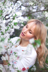 Young brunette woman posing in blooming white apple flowers on branches