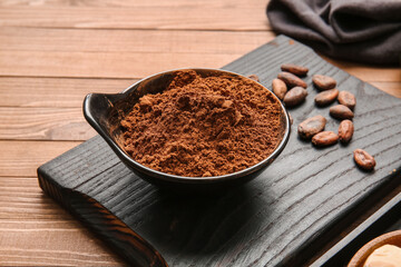 Bowl with cocoa powder and beans on wooden background