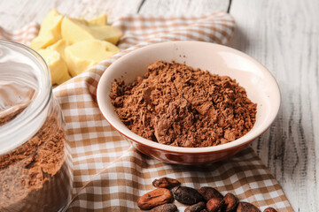Bowl with cocoa powder on light wooden background