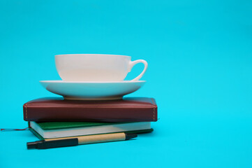 A notebook and pen, a cup of coffee, are stacked on a blue background.