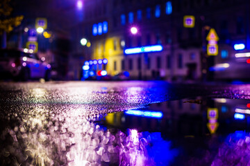 Autumn rainy night in the city. Empty street. Parked cars. Residential buildings in the city center. Colorful colors. Close up view from the level of the puddle on the pavement.