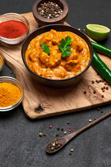 Black ceramic bowl of Traditional Chicken Curry and spices on dark concrete background