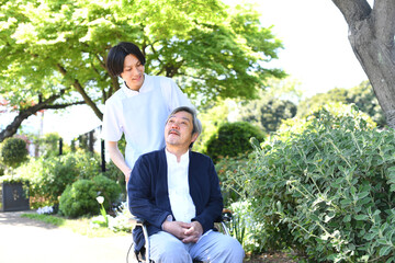 屋外で散歩をする介護ヘルパーの男性と車椅子のシニア男性
