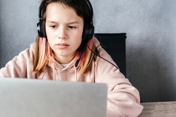 A girl wearing headphones and using her laptop while studying online, e-learning and online...